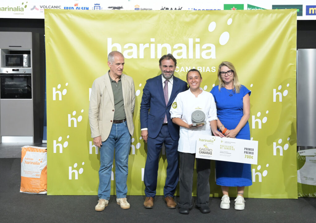 Group of four adults posing with a trophy and certificate in front of a yellow Harinalia backdrop at an awards event.