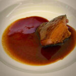 Braised beef in a rich brown sauce on a white plate, shown from a close angle.