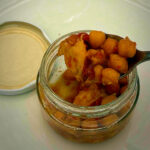 Golden fried chickpeas in a glass jar with a creamy dip nearby on a light surface