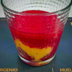 Layered red and yellow cocktail in a textured clear glass on a dark surface, close-up view.
